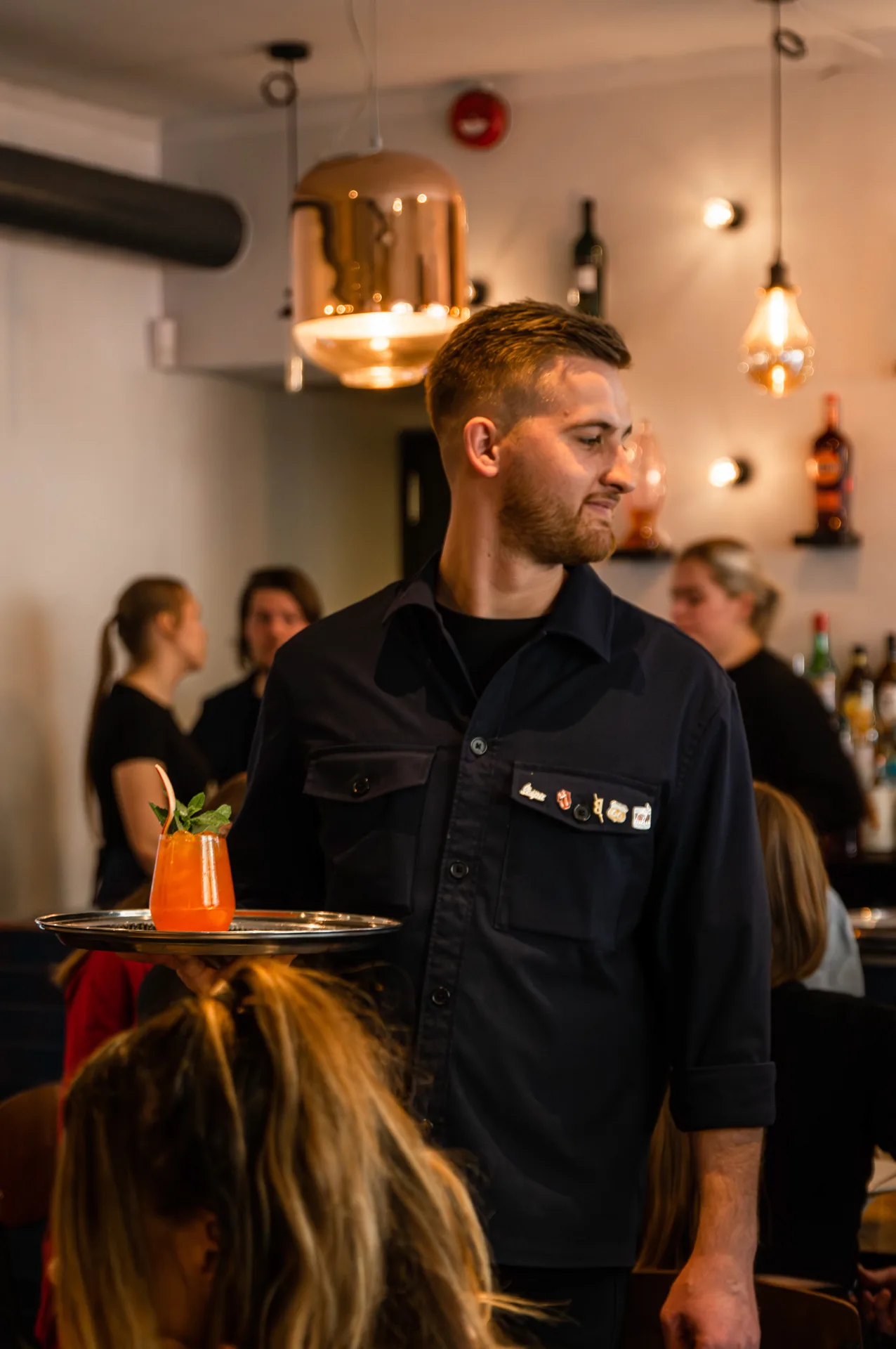 Teenindaja viib kandikuga kohtunikele erimenüü kokteili Tartu Cocktail Week, pildistas Tartu fotograaf Mailis Vahenurm Foto kelnerist sündmuselt Tartu Cocktail Week elustiili restoranis Pepe's, pildistas ürituste fotograaf Mailis Vahenurm.
